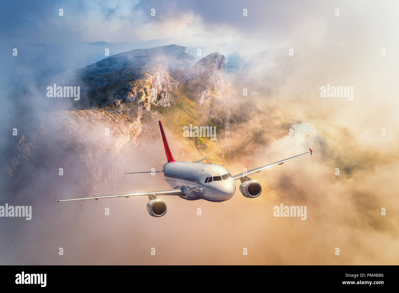 Vol d'un avion au-dessus de montagnes et nuages bas au coucher du soleil en Espagne. Paysage avec des avions de passagers, ciel nuageux, des rochers, des forêts et du soleil. Business Banque D'Images