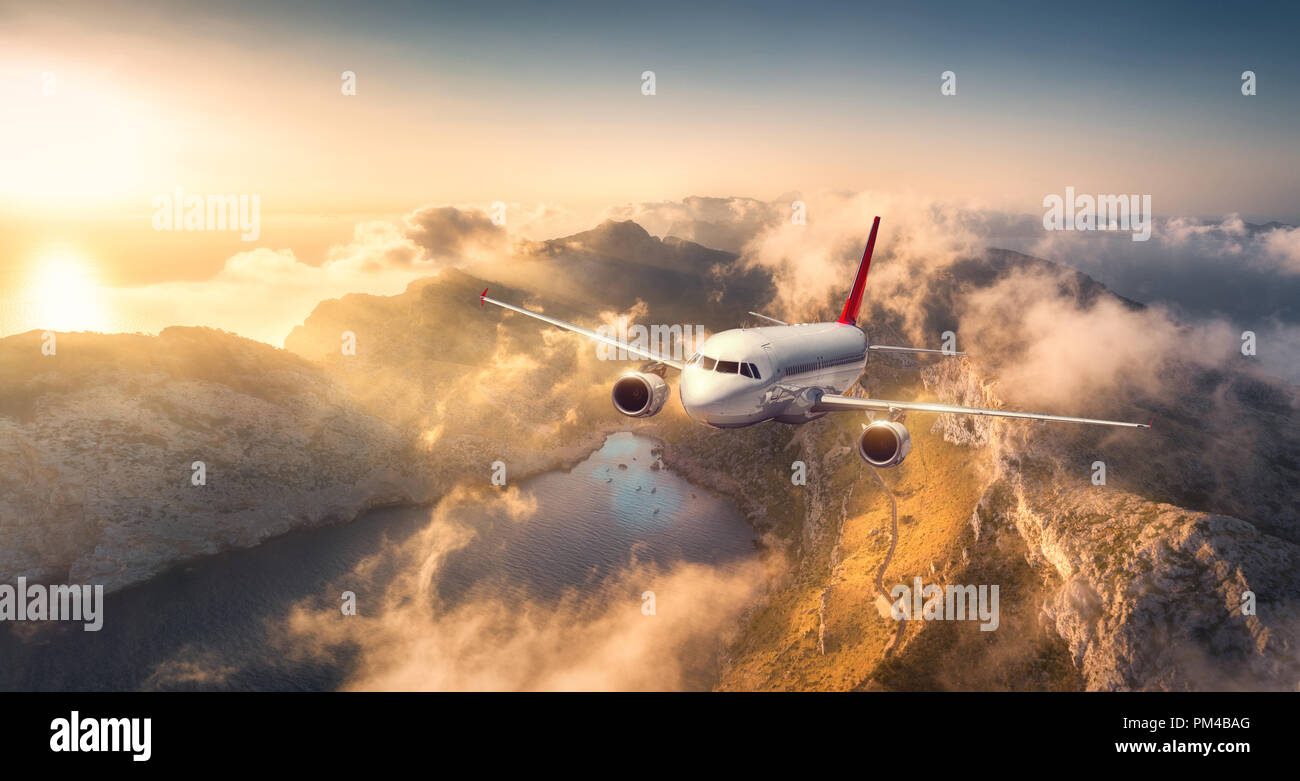 Vol d'un avion au-dessus de montagnes et nuages bas au coucher du soleil en Espagne. Paysage avec des avions de passagers, ciel nuageux, des rochers, des forêts et du soleil. Business Banque D'Images