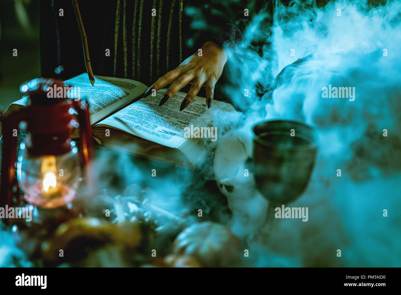 Close-up of a witch's part avec des clous noir fumé sur livre de recette magique et avec une baguette magique. Banque D'Images