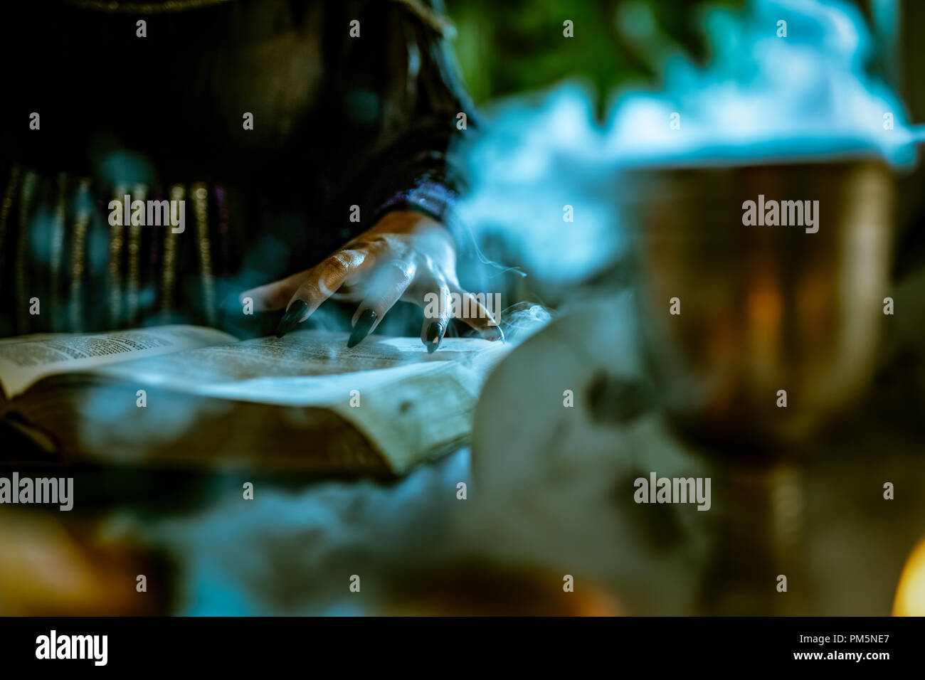 Close-up of a witch's part avec des clous noir fumé sur livre de recette magique et avec une baguette magique. Banque D'Images