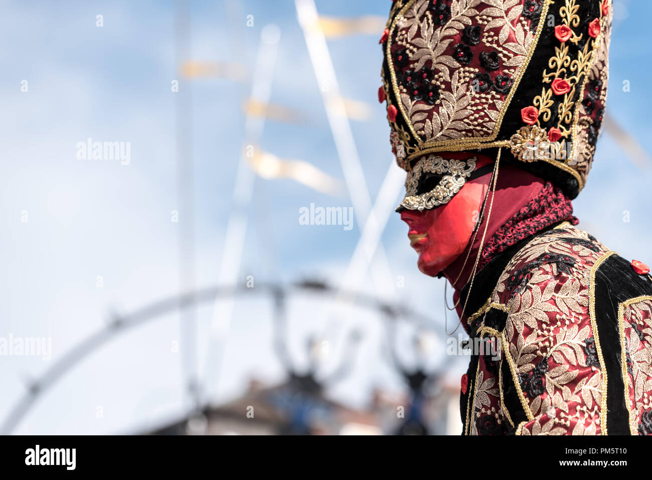 Homme dans un masque rouge et or, un carnaval vénitien traditionnel costume sur fond de ciel bleu Banque D'Images