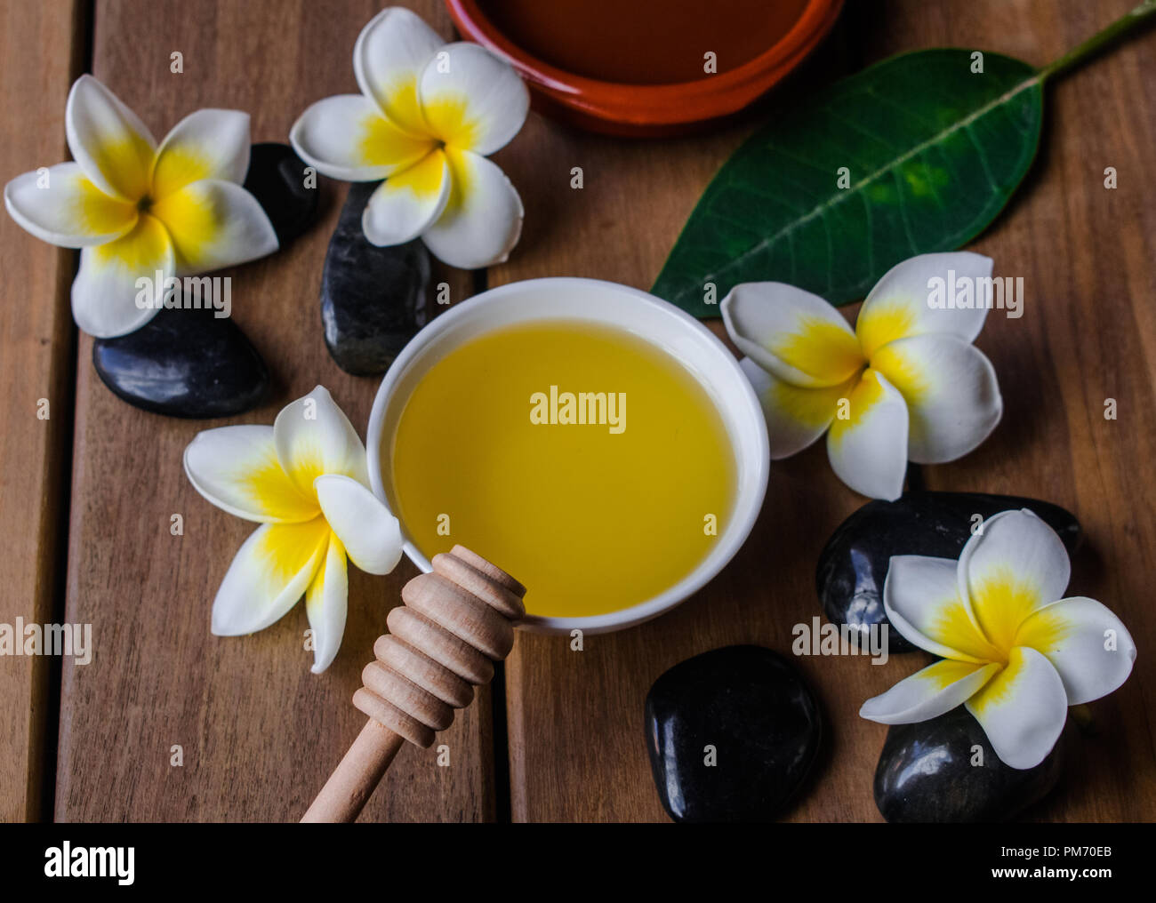 Huile de Massage au miel cuillère en bois avec fleurs de plumeria et noir pierres rondes sur la surface en bois Banque D'Images
