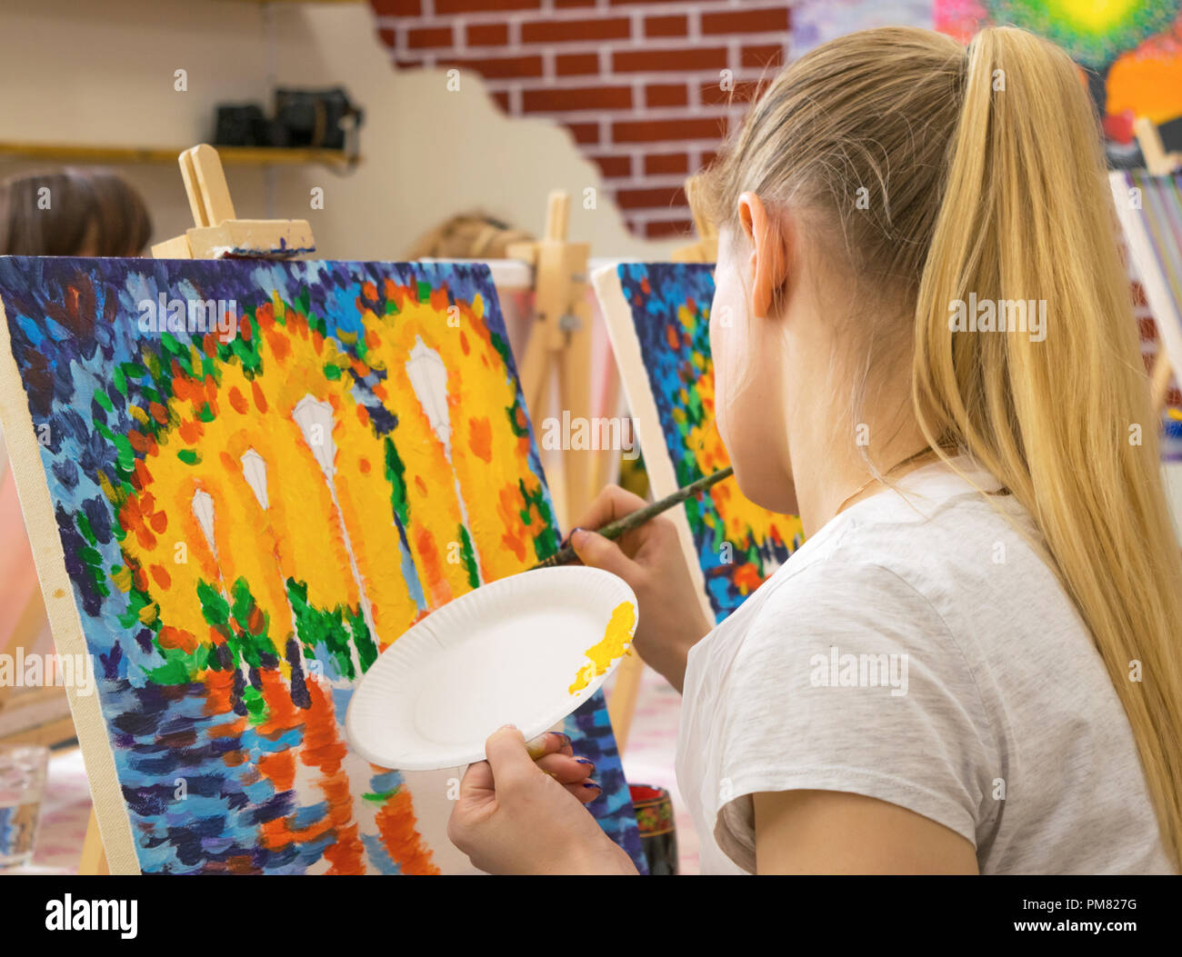 Jeune femme avec une longue chevelure blonde s'appuyant sur une toile au cours de maître dans l'art studio Banque D'Images