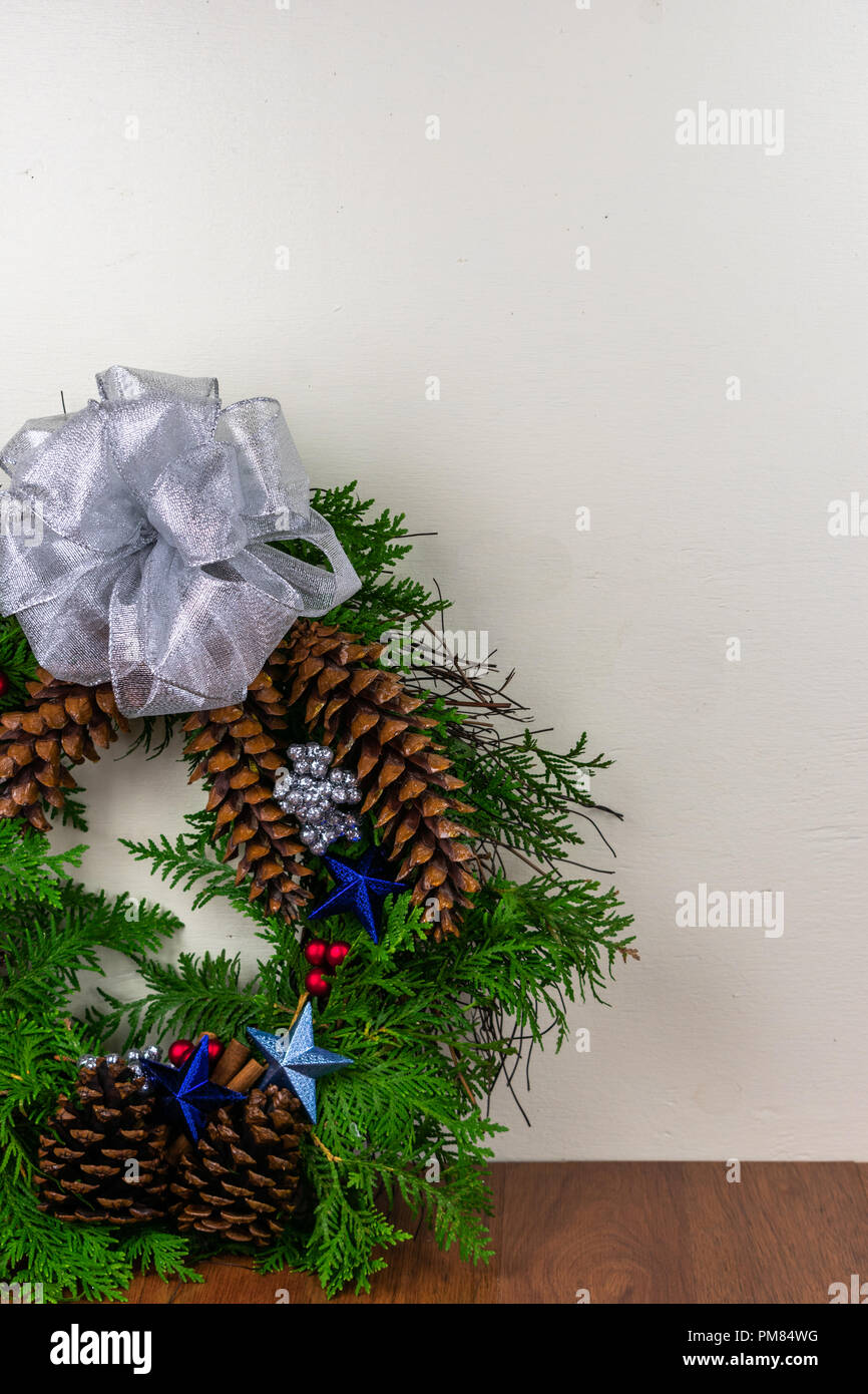 Une couronne de Noël avec des branches de cèdre, pommes de pin, des bâtons de cannelle, blue stars, fruits rouges, et d'argent des grappes de petits fruits avec un arc d'argent sur le dessus Banque D'Images