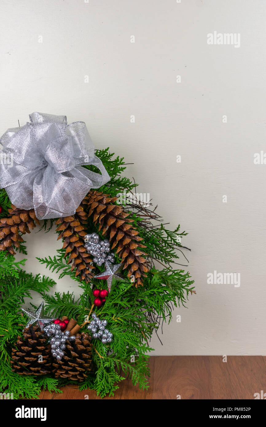 Une couronne de Noël avec des branches de cèdre, pommes de pin, des bâtons de cannelle, les étoiles d'argent, les fruits rouges, et d'argent des grappes de petits fruits avec un arc d'argent sur le dessus Banque D'Images