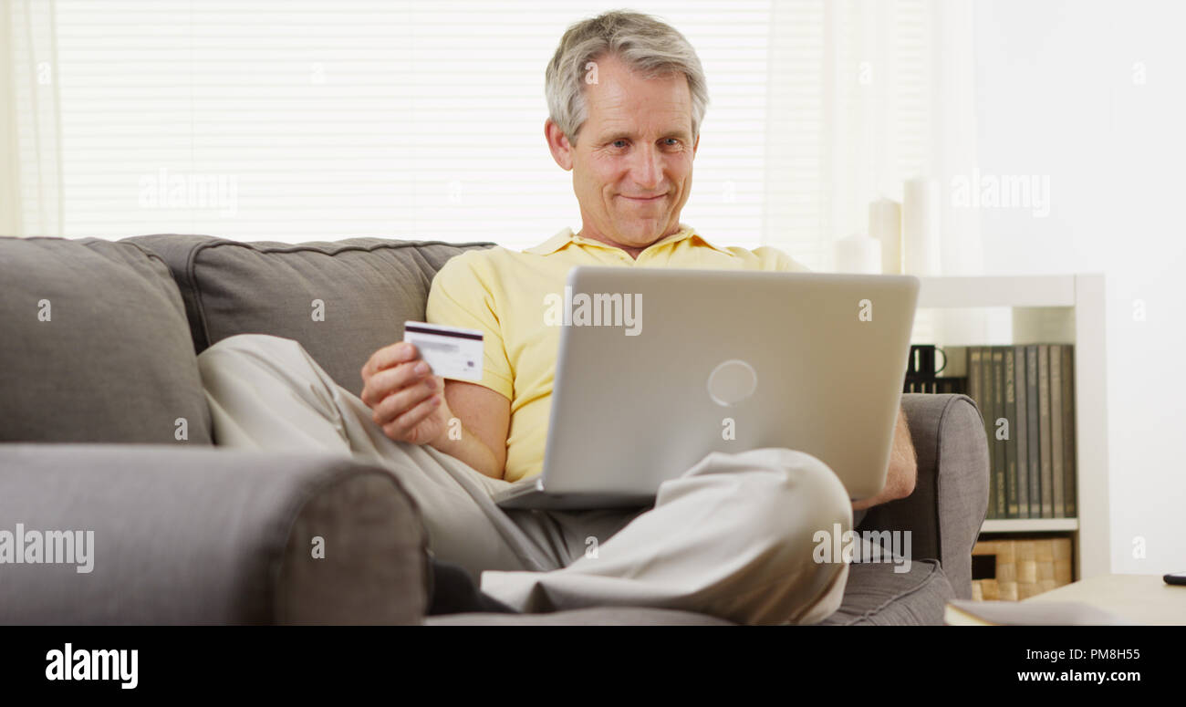 Pris sa retraite happy middle-aged man holding carte de crédit pour effectuer un achat d'un ordinateur portable Banque D'Images