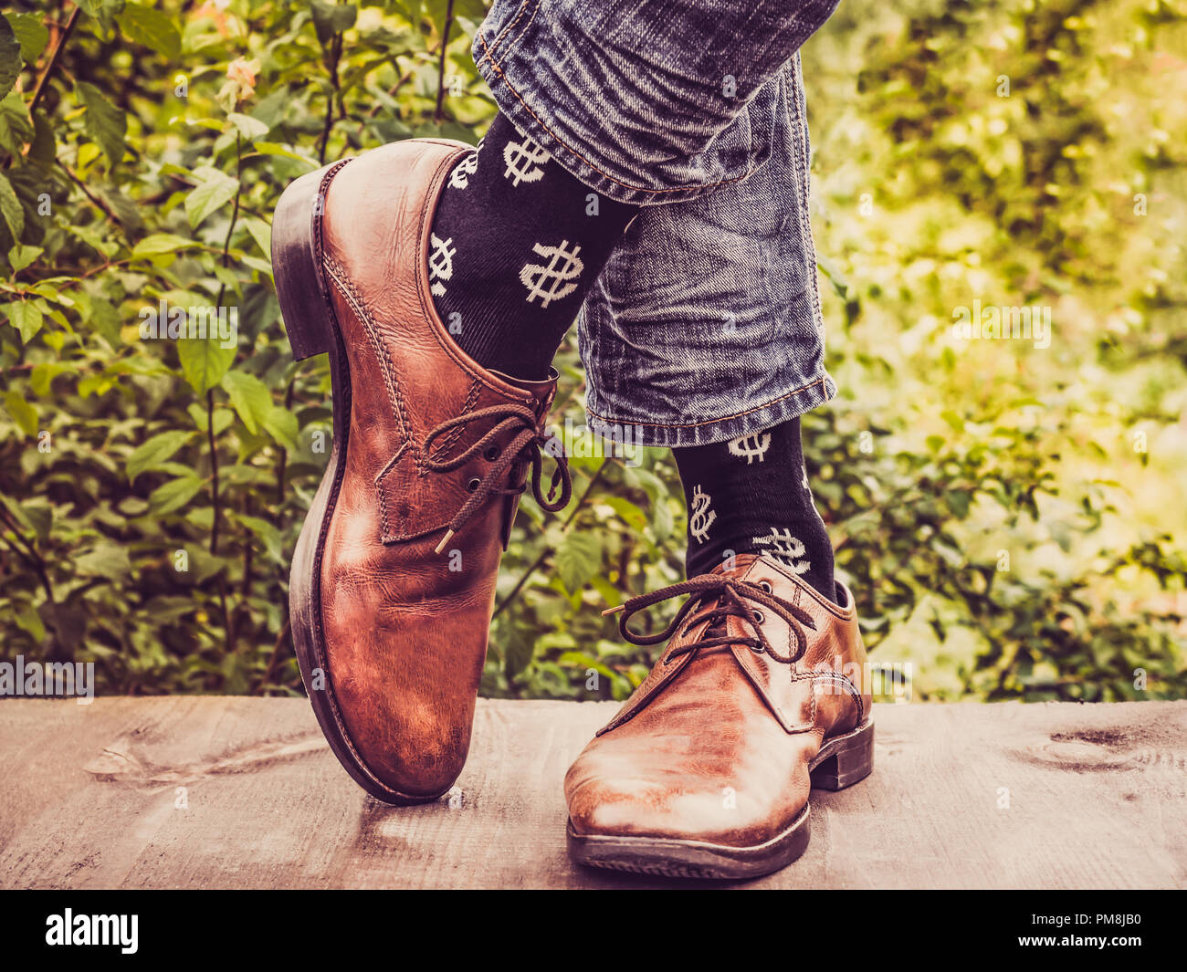 Les jambes de l'homme dans l'élégant quartier de chaussures, chaussettes  noirs avec des motifs en forme de dollars US sur une terrasse en bois dans  le contexte des arbres verts. Beauté, fa