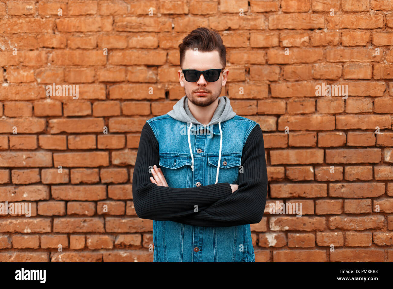 Portrait d'un homme dans un beau hipster gilet en jean près d'un mur de briques Banque D'Images