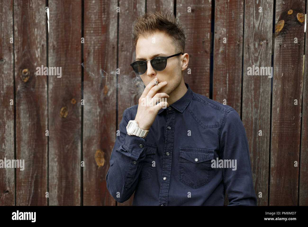 L'homme élégant fume une cigarette et souffle la fumée près de un mur vintage. Banque D'Images