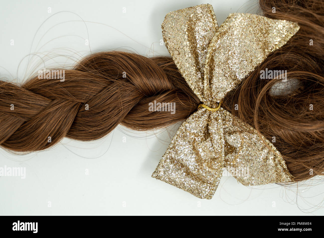 De beaux cheveux bruns tressés isolé sur blanc, cuir gold bow jointe à la fin de la tresse. Banque D'Images