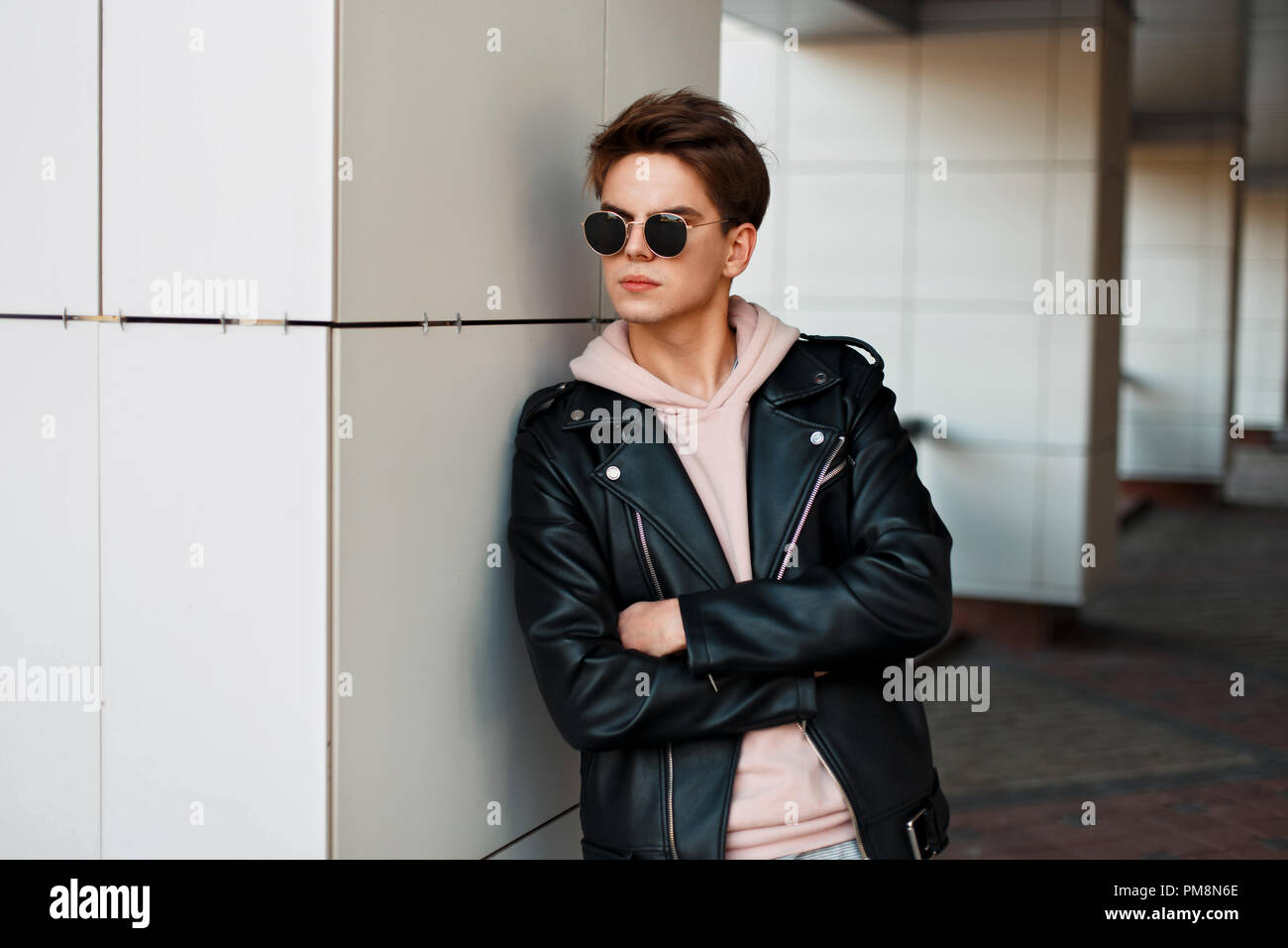 Beau jeune mec avec des lunettes de soleil dans un quartier à la mode veste  de marque se tient près d'un mur blanc Photo Stock - Alamy