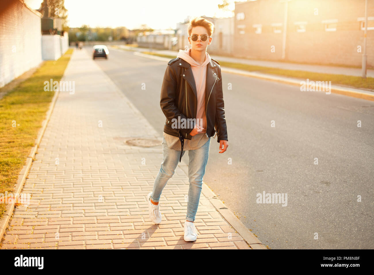 Bel homme dans un manteau de cuir noir et blanc chaussures de marche dans  la rue au coucher du soleil Photo Stock - Alamy