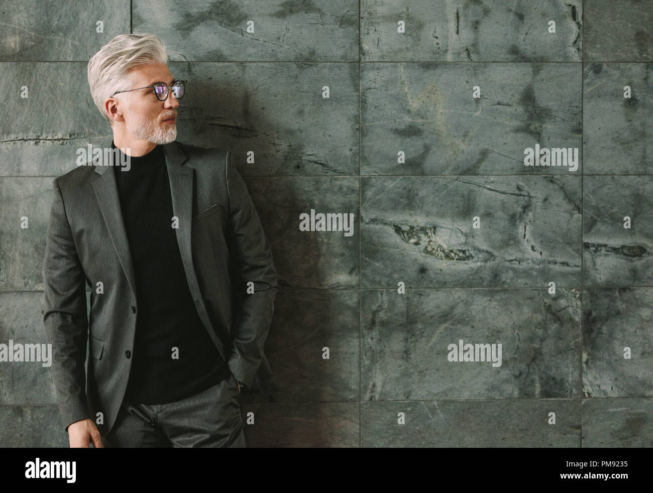 Portrait of handsome man en tenue à l'hôtel. Senior businessman standing contre mur gris avec copie espace. Banque D'Images