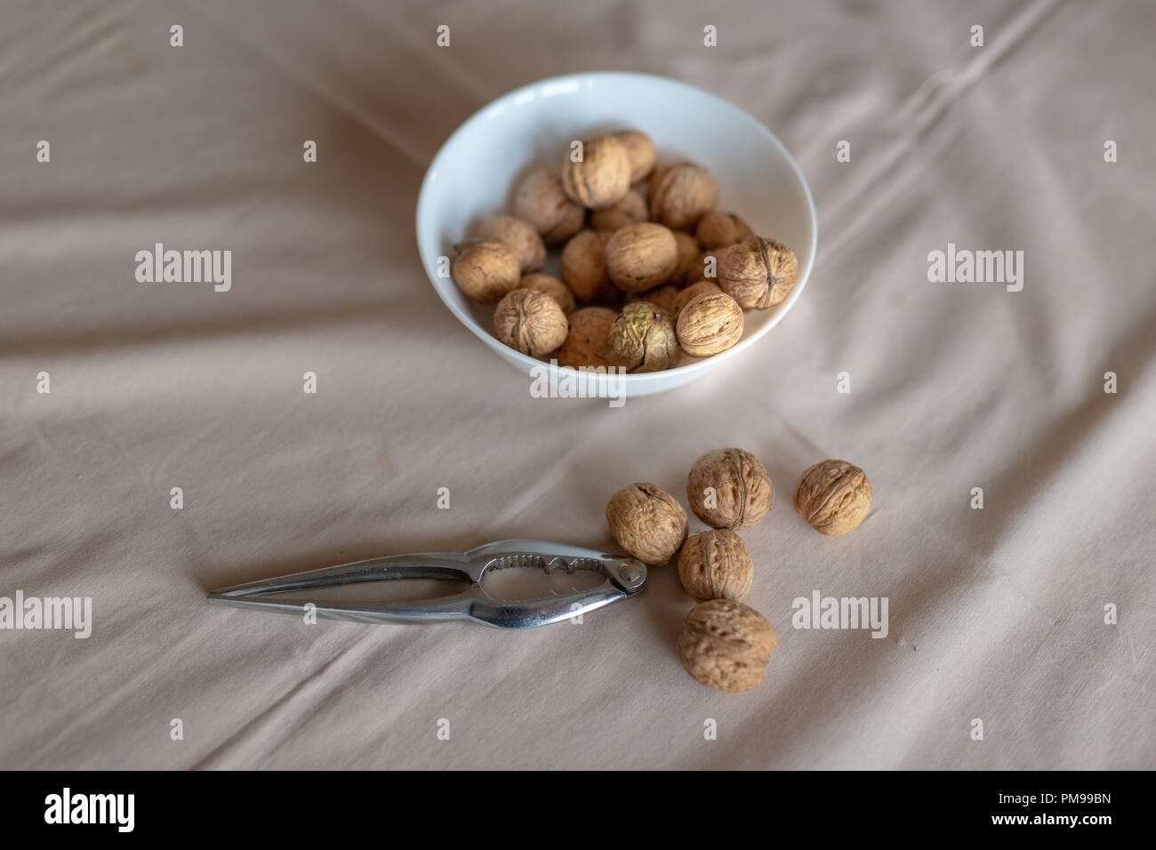Casse-noisette et les noix dans un bol sur une table couverte d'une nappe. En-cas sur la table de cuisine. Fond clair. Banque D'Images