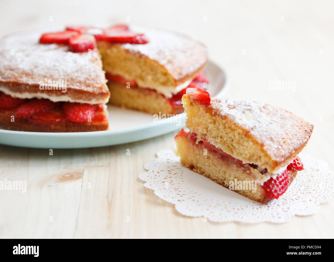 Gâteau éponge Victoria avec des fraises, confiture et crème fouettée avec une pièce sur une table en bois Banque D'Images