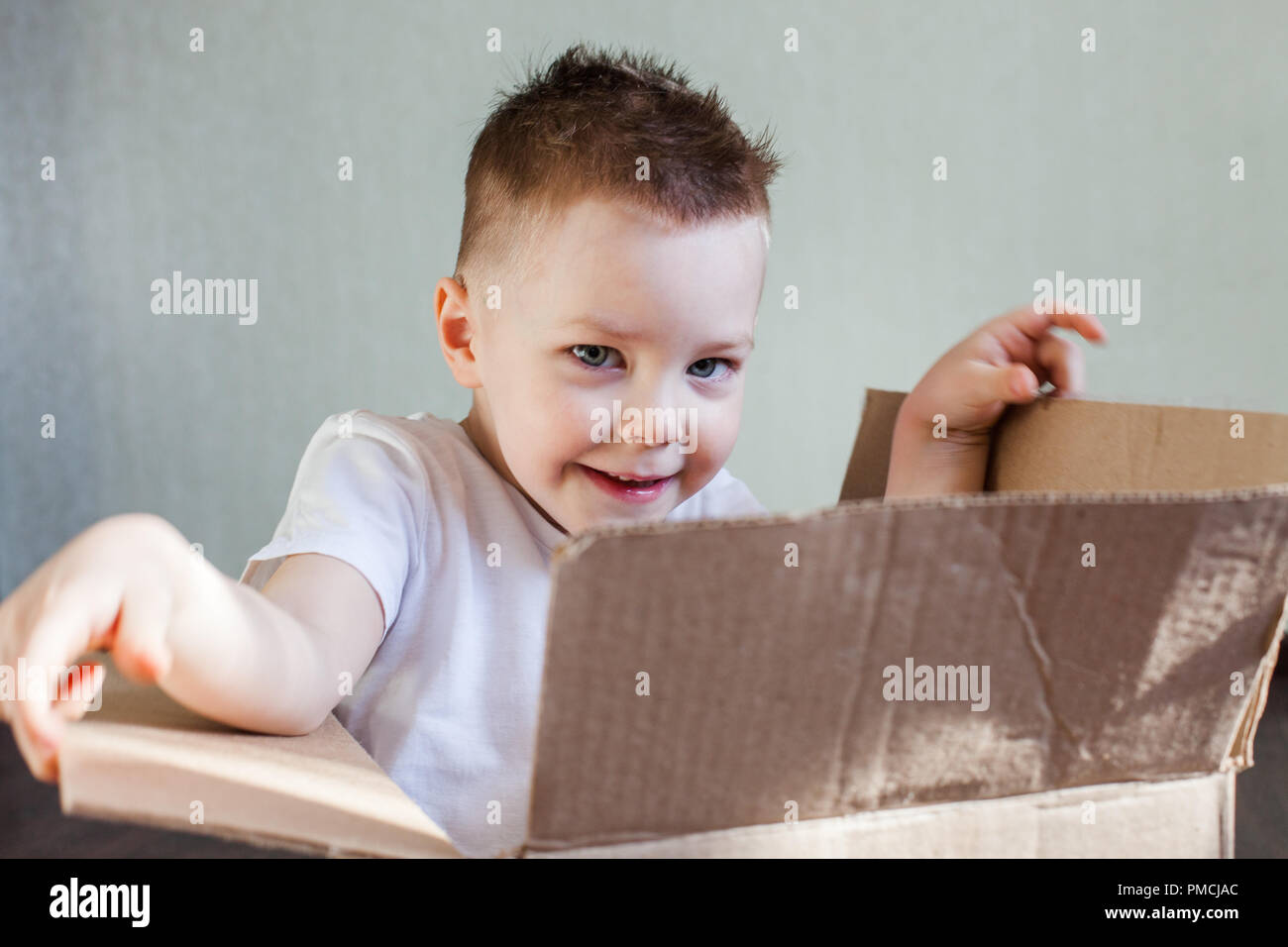 Un garçon blond de 4 ans se trouve dans une boîte en carton à la maison et joue à cache-cache, pick a boo Banque D'Images
