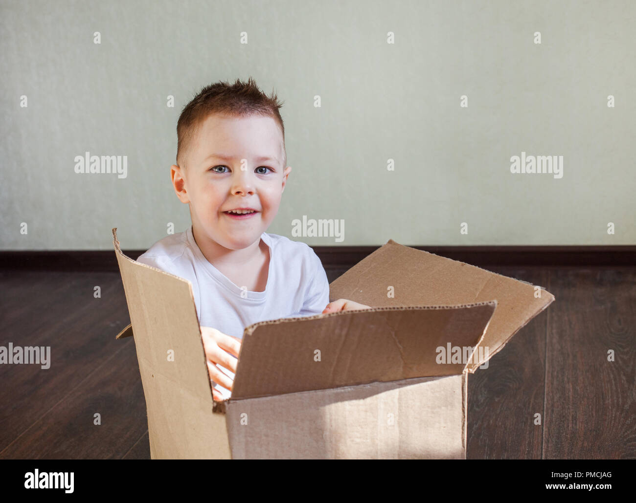 Garçon 4 ans homme blond assis dans une boîte en carton à la maison et souriant, sincère émotion et plaisir Banque D'Images