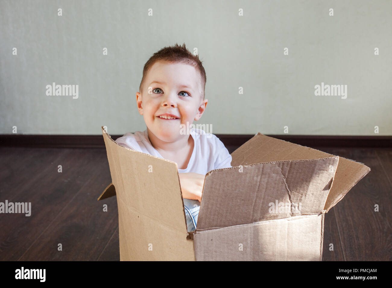 Garçon 4 ans homme blond assis dans une boîte en carton à la maison et souriant, sincère émotion et plaisir Banque D'Images