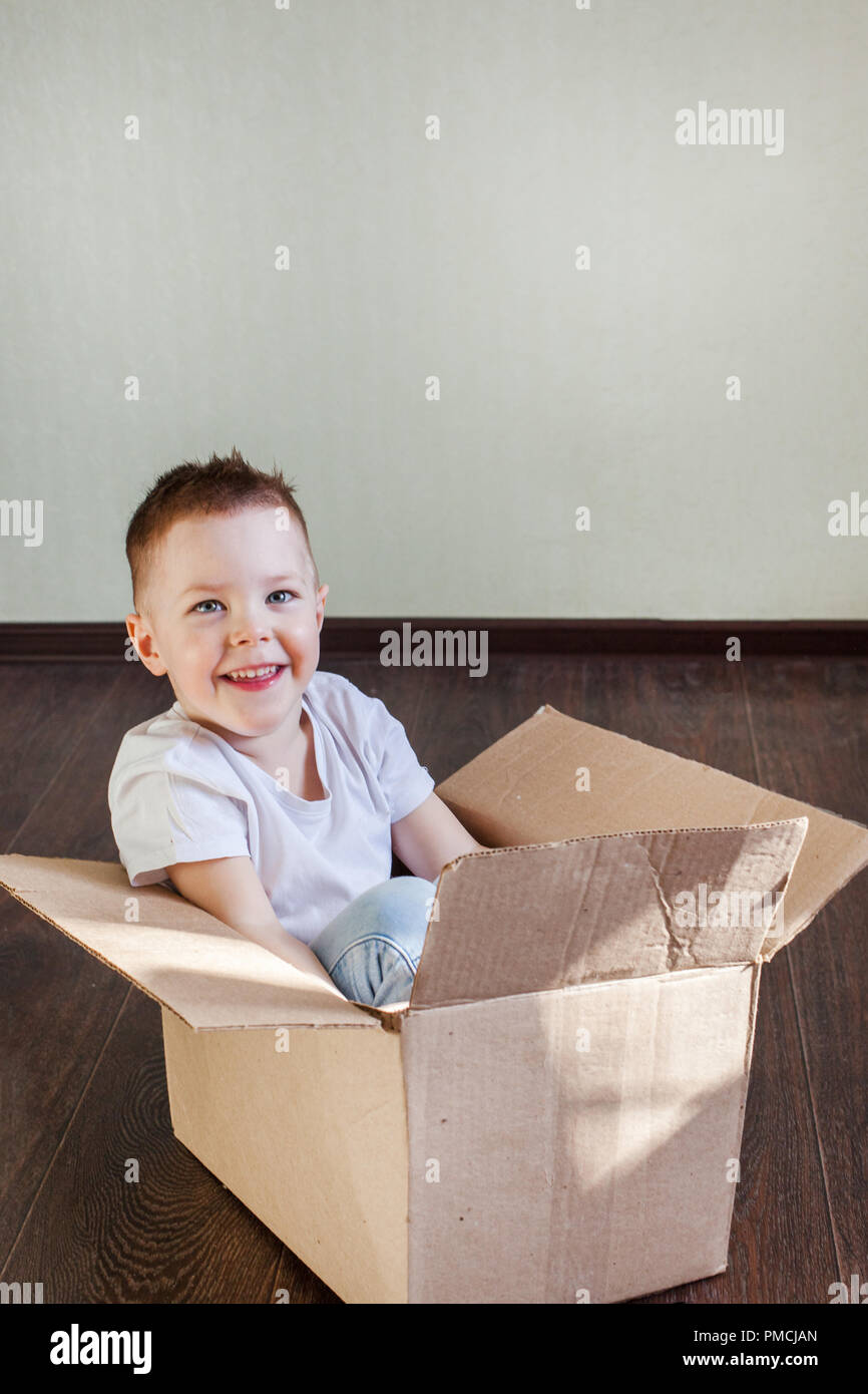 Garçon 4 ans homme blond assis dans une boîte en carton à la maison et souriant, sincère émotion et plaisir Banque D'Images