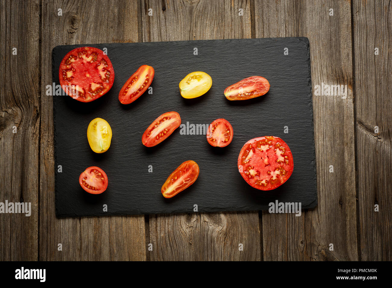 Variété de tomates fraîches mûres jardinage biologique différents types et couleurs spot avec de l'eau et les feuilles de basilic dans le bac en bois sur fond de bois gris ancien. Mise à plat, de l'espace Banque D'Images