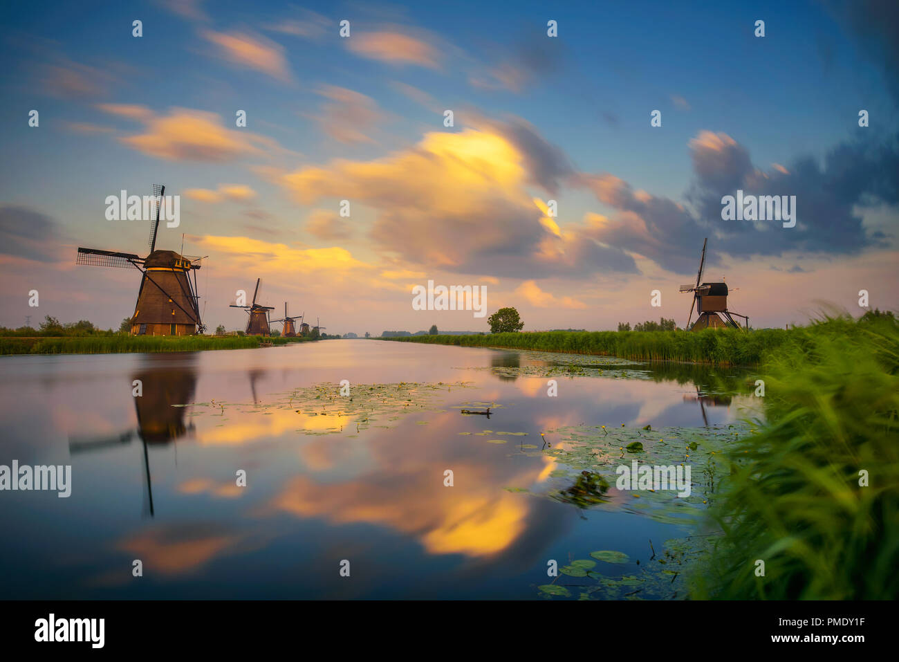 Coucher du soleil au-dessus de vieux moulins à vent hollandais et une rivière qui coule par à Kinderdijk, Pays-Bas. Longue exposition. Banque D'Images