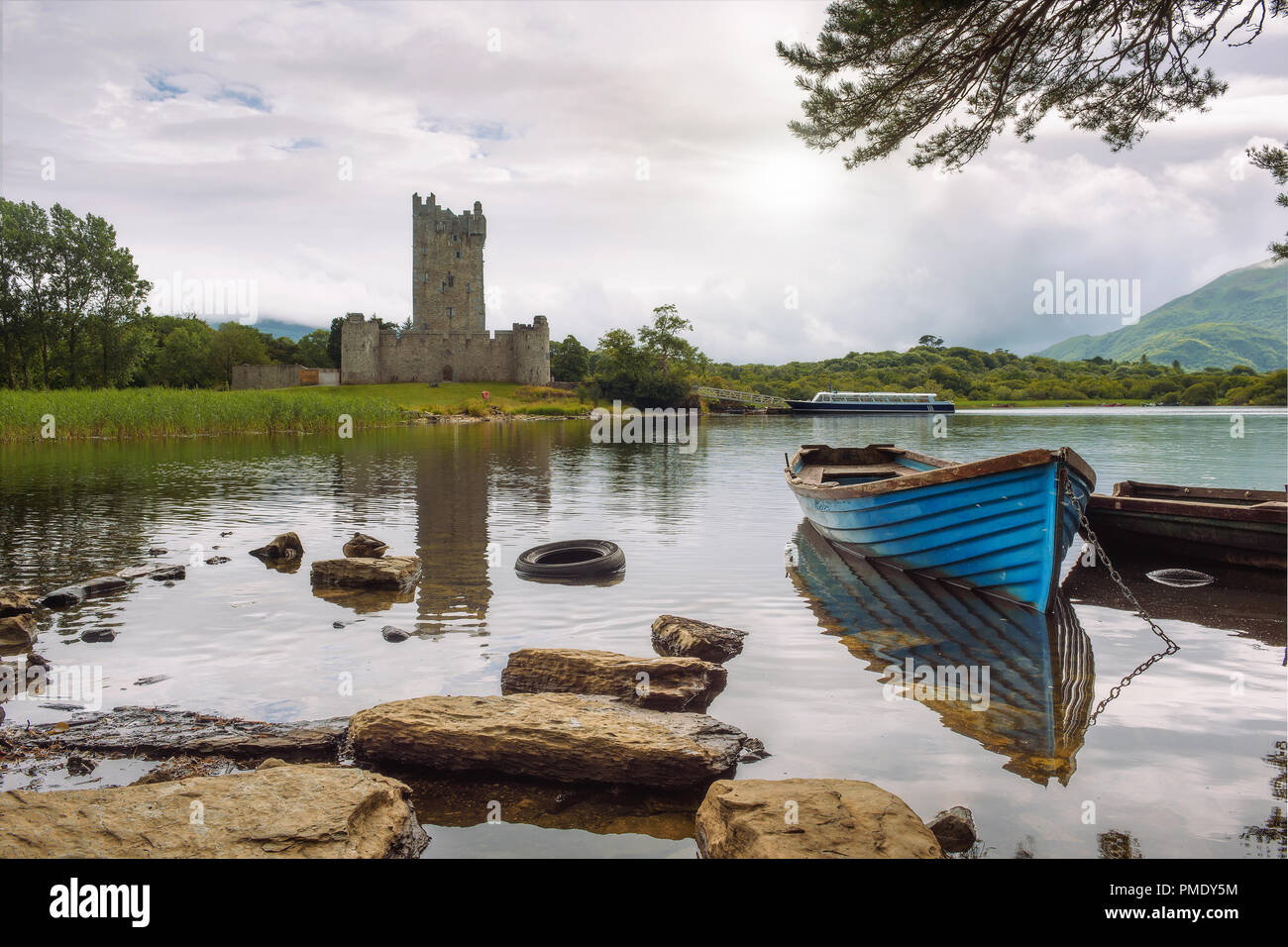 Ruines du Château de Ross et le Lough Leane lac avec un bateau bleu à l'avant-plan dans le Parc National de Killarney, Irlande Banque D'Images