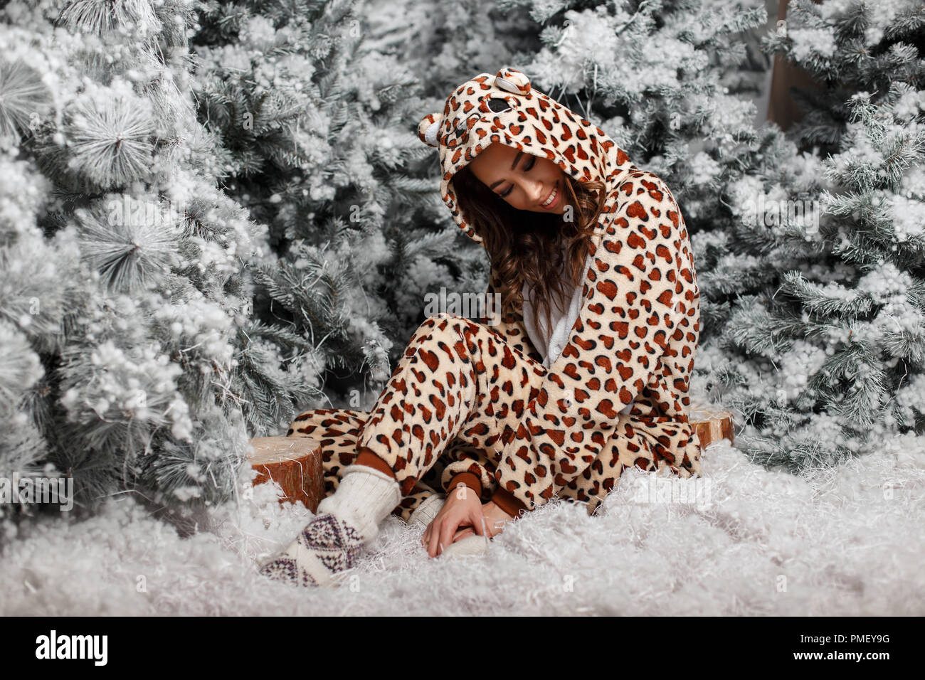 Belle jeune fille heureuse dans Drôle de pyjama ours assis près de l'arbre de Noël avec de la neige Banque D'Images