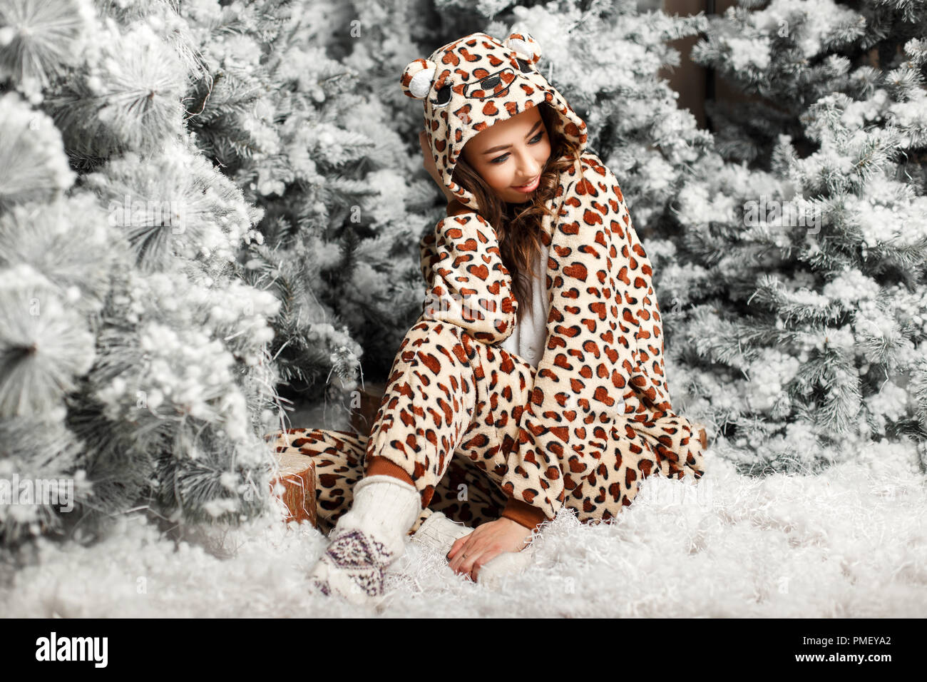 Happy cute girl dans un quartier branché de pyjama ours assis près d'un arbre de Noël Banque D'Images