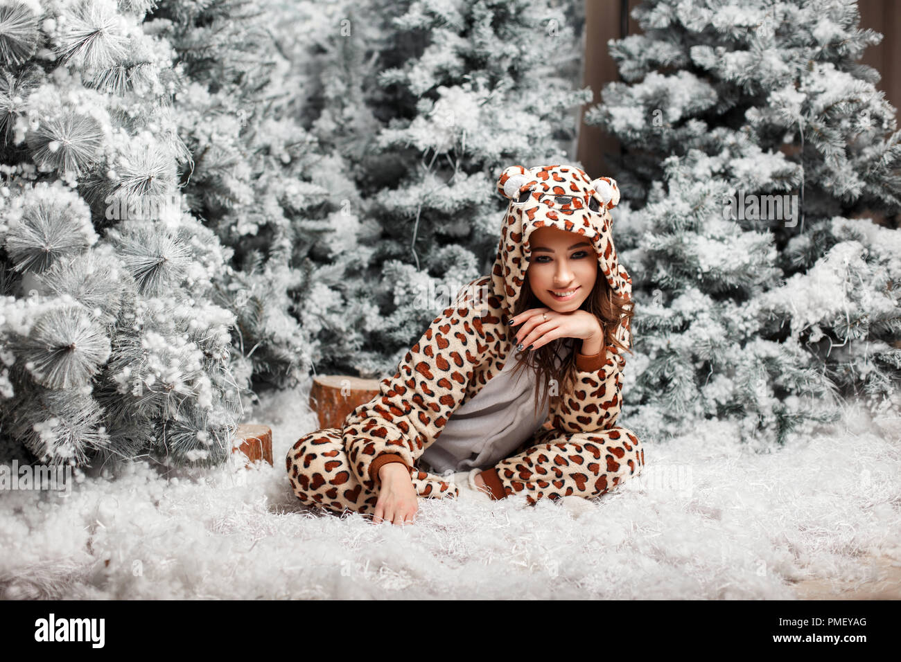 Funny happy woman in a trendy pyjama ours assis près d'un arbre de Noël avec de la neige dans le studio Banque D'Images