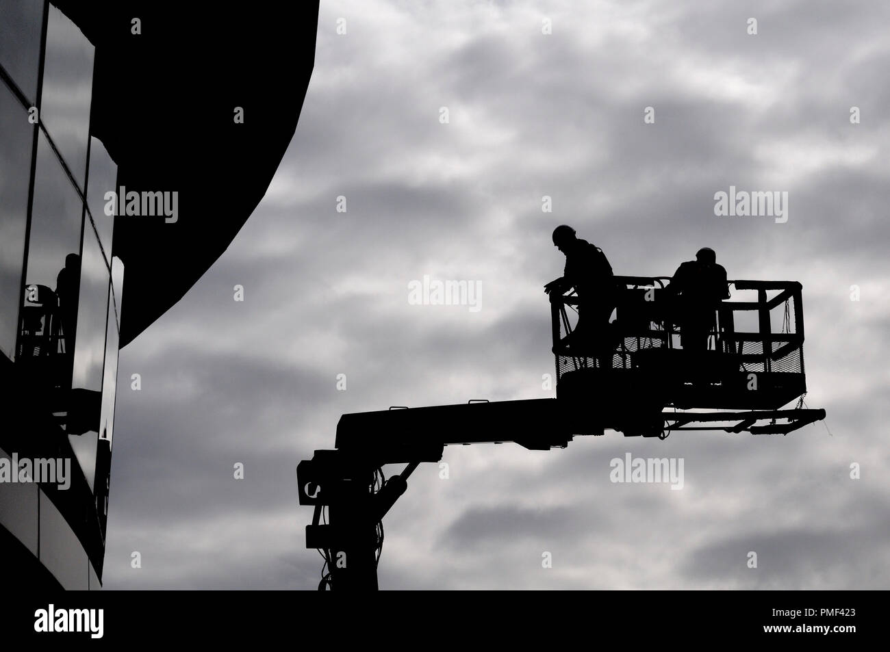Deux travailleurs de la construction en silhouette contre le ciel gris sur une rampe de levage hydraulique Banque D'Images