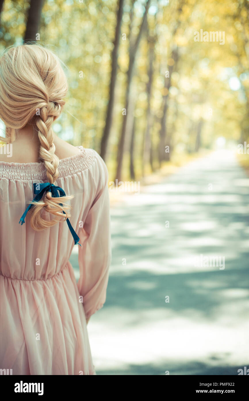 Femme blonde en robe rose debout à l'automne country road Banque D'Images