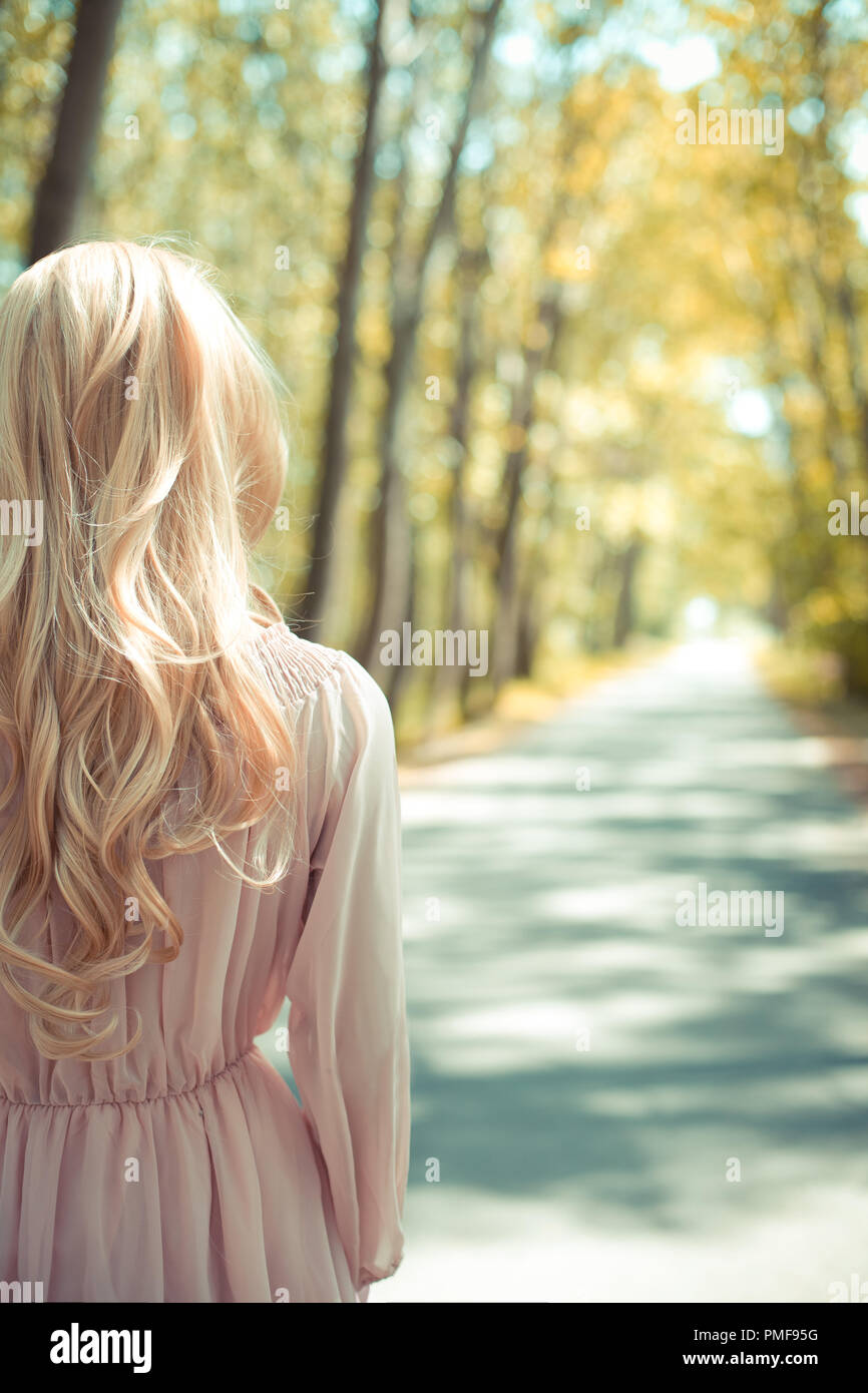 Femme blonde en robe rose debout à l'automne country road Banque D'Images