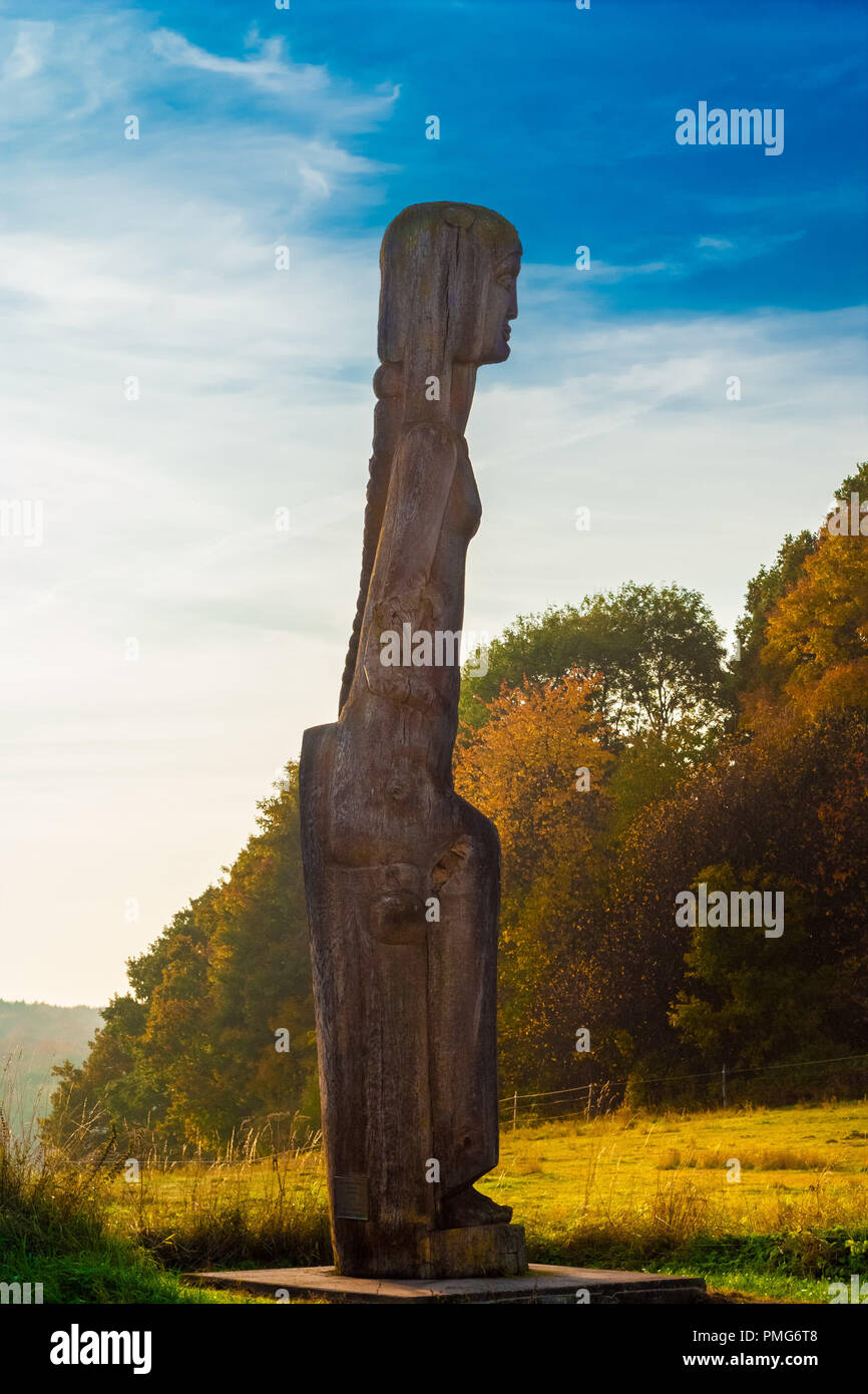 Une belle sculpture en bois d'une femme assise près de la lisière de la forêt de Reinhardswald en Allemagne sur une belle journée d'automne doré. Banque D'Images