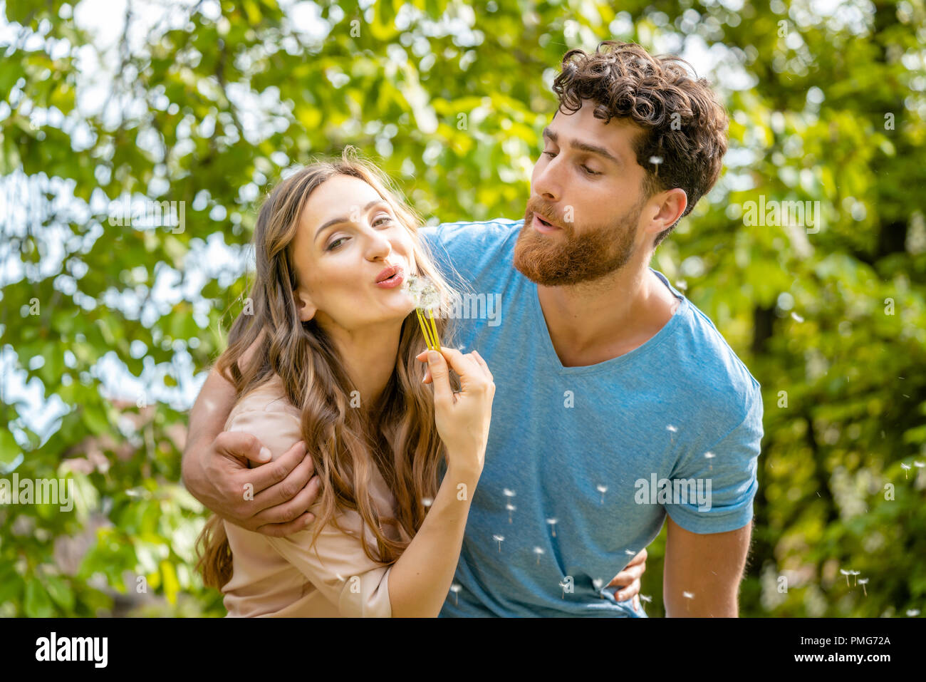 Jeune couple à rêver de leur avenir blowing dandelion seeds Banque D'Images
