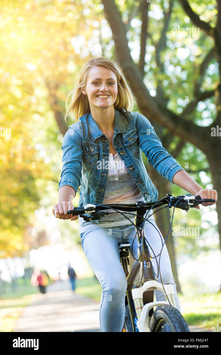 Jeune femme faire du vélo dans le parc de l'automne. Tout en appréciant à vélo dans la nature au cours de journée d'automne. Banque D'Images
