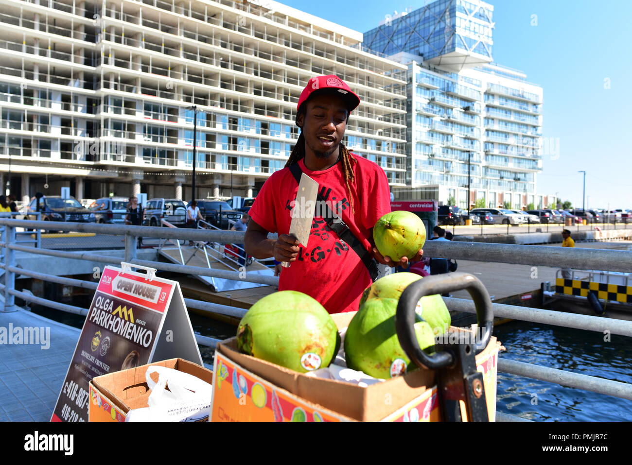 Un jeune vendeur de rue noir vend des mangues sur la rue, à côté d'une enseigne immobilière de l'annonce d'un 'Open House' pour une propriété. Banque D'Images