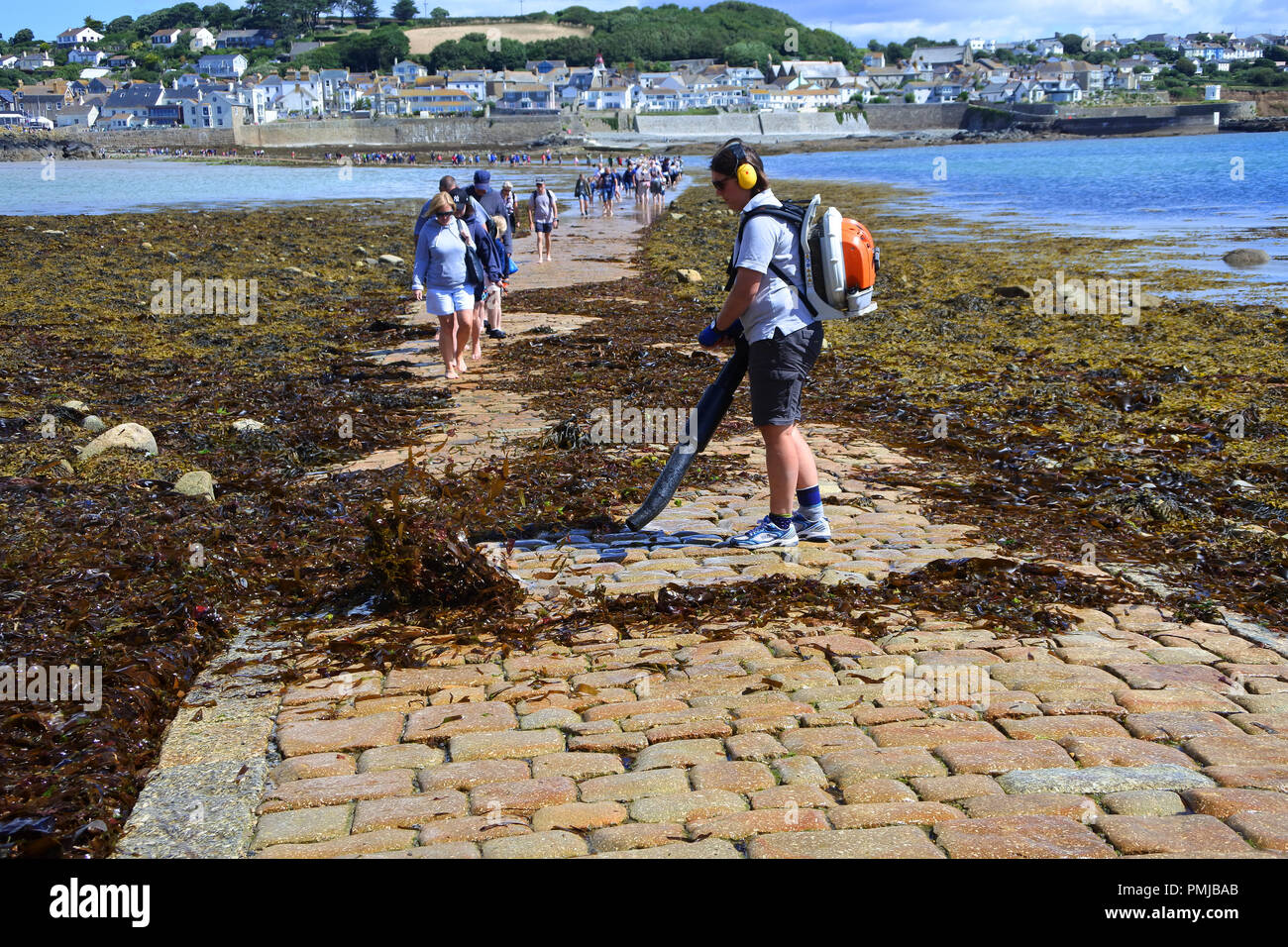 Jardinier femelle soufflant algues marines l'ouverture causeway comme des foules de touristes à pied de St Michael's Mount, Cornwall, UK - John Gollop Banque D'Images