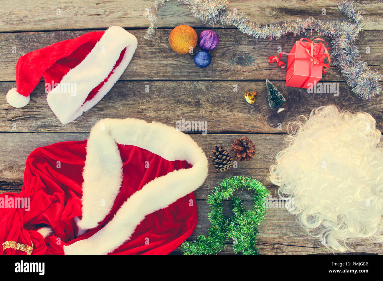 Costume Père Noël, petit arbre, pomme de pin, des boules de Noël, guirlande, cadeau sur fond de bois. Vue d'en haut. La tonalité de l'image. Banque D'Images