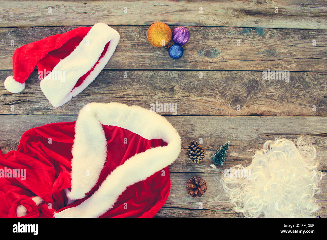 Costume Père Noël, petit arbre, pomme de pin, des boules de Noël, guirlande, cadeau sur fond de bois. Vue d'en haut. La tonalité de l'image. Banque D'Images