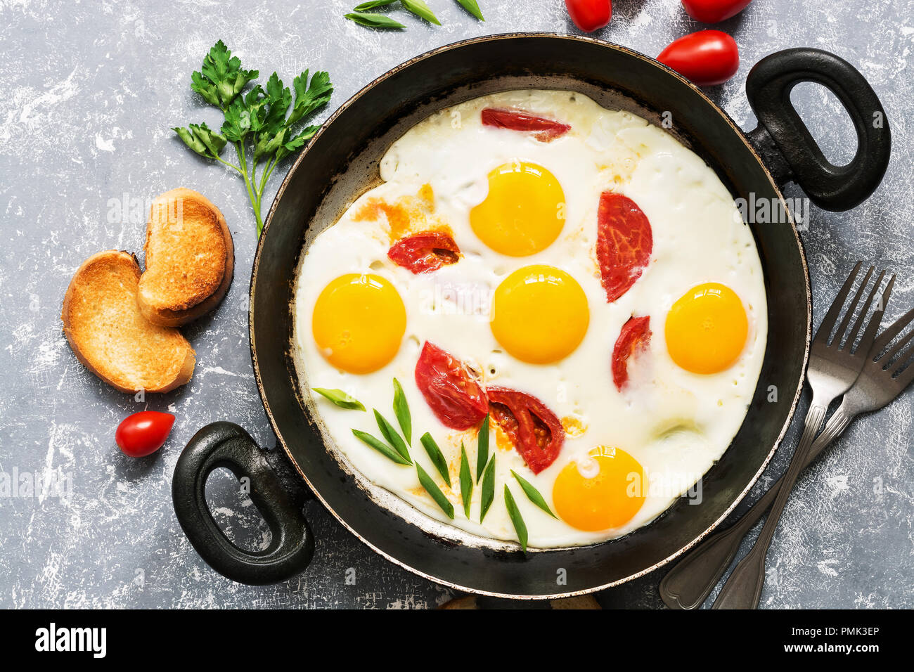 Oeufs au plat avec les tomates dans une poêle, fond gris.Télévision. Banque D'Images