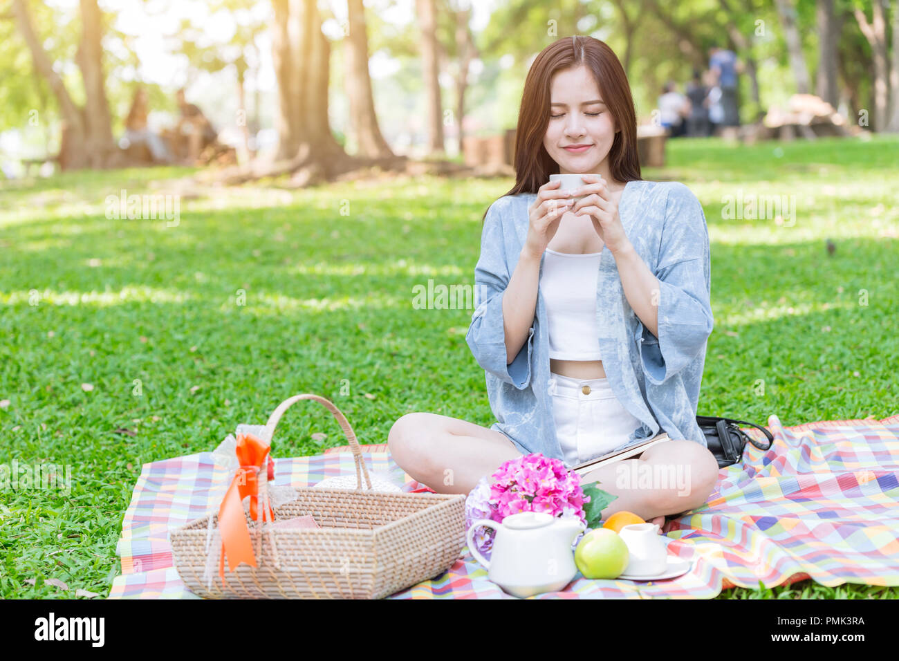 Cute teen boire du lait chaud tandis que le tapis de pique-nique assis sur Green Park maison de plein air se détendre. Banque D'Images