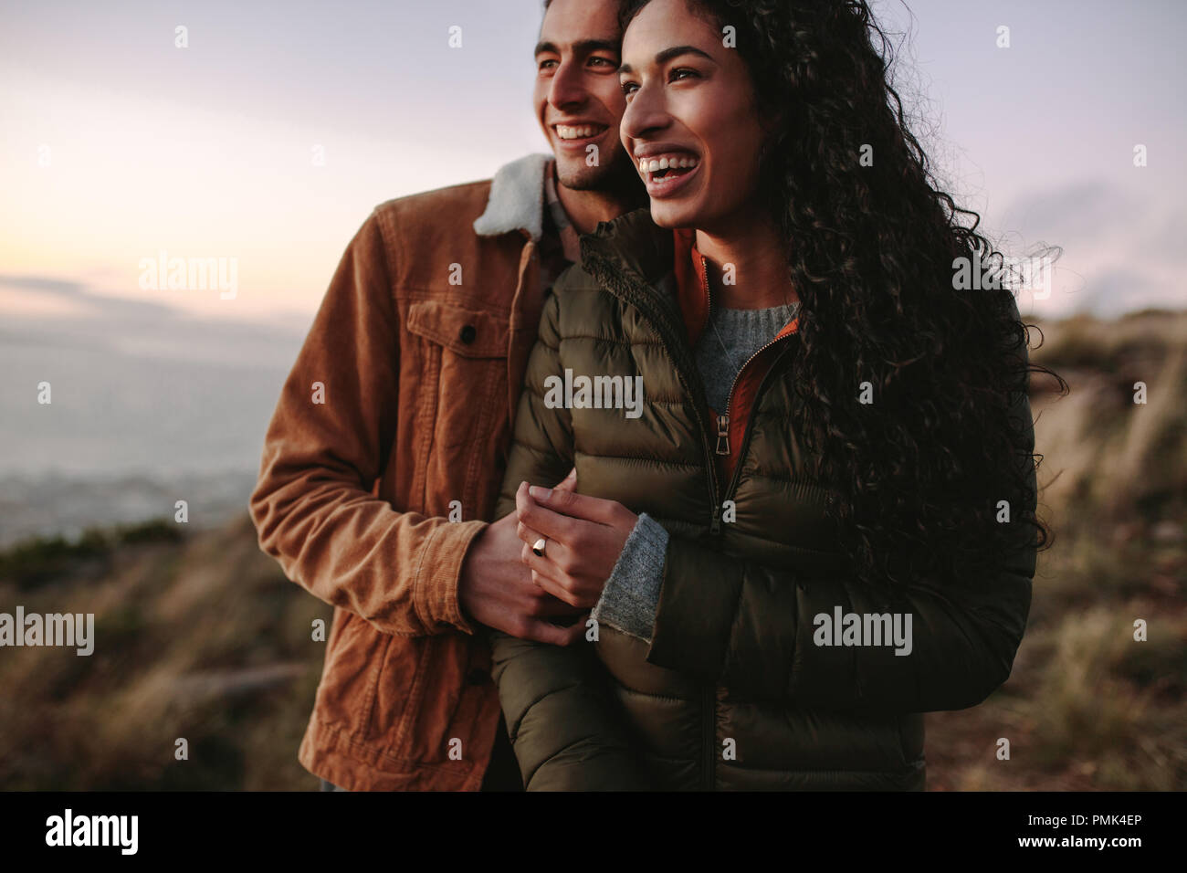 couple de voyage en hiver porter debout dehors ensemble sur la falaise et regardant la vue. Homme et femme regardant la vue du sommet de la montagne et riant Banque D'Images