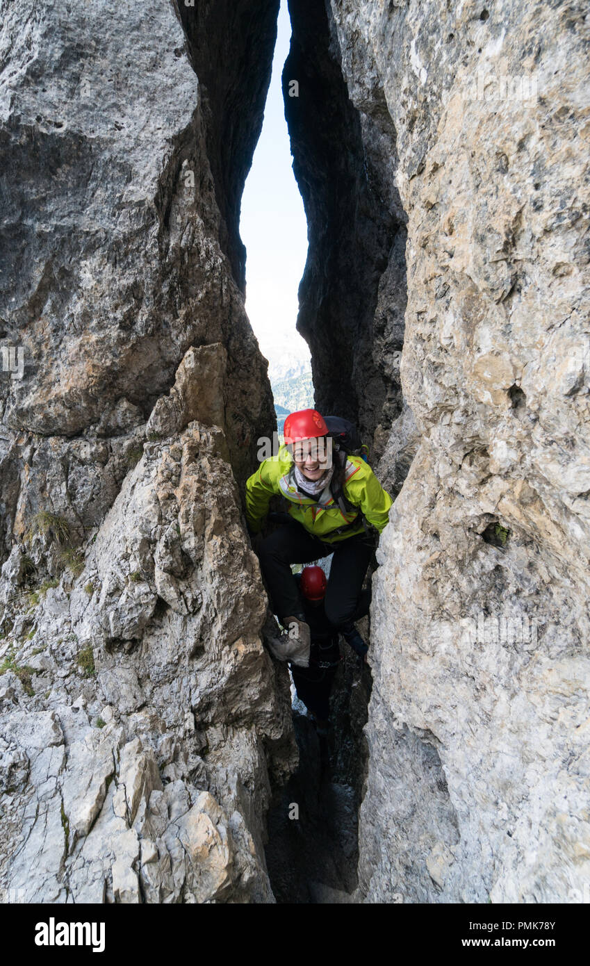 Deux jeunes femmes montain grimpeurs passer par une étroite fissure sur une montée raide dans les Dolomites d'Alta Badia en Italie du nord Banque D'Images