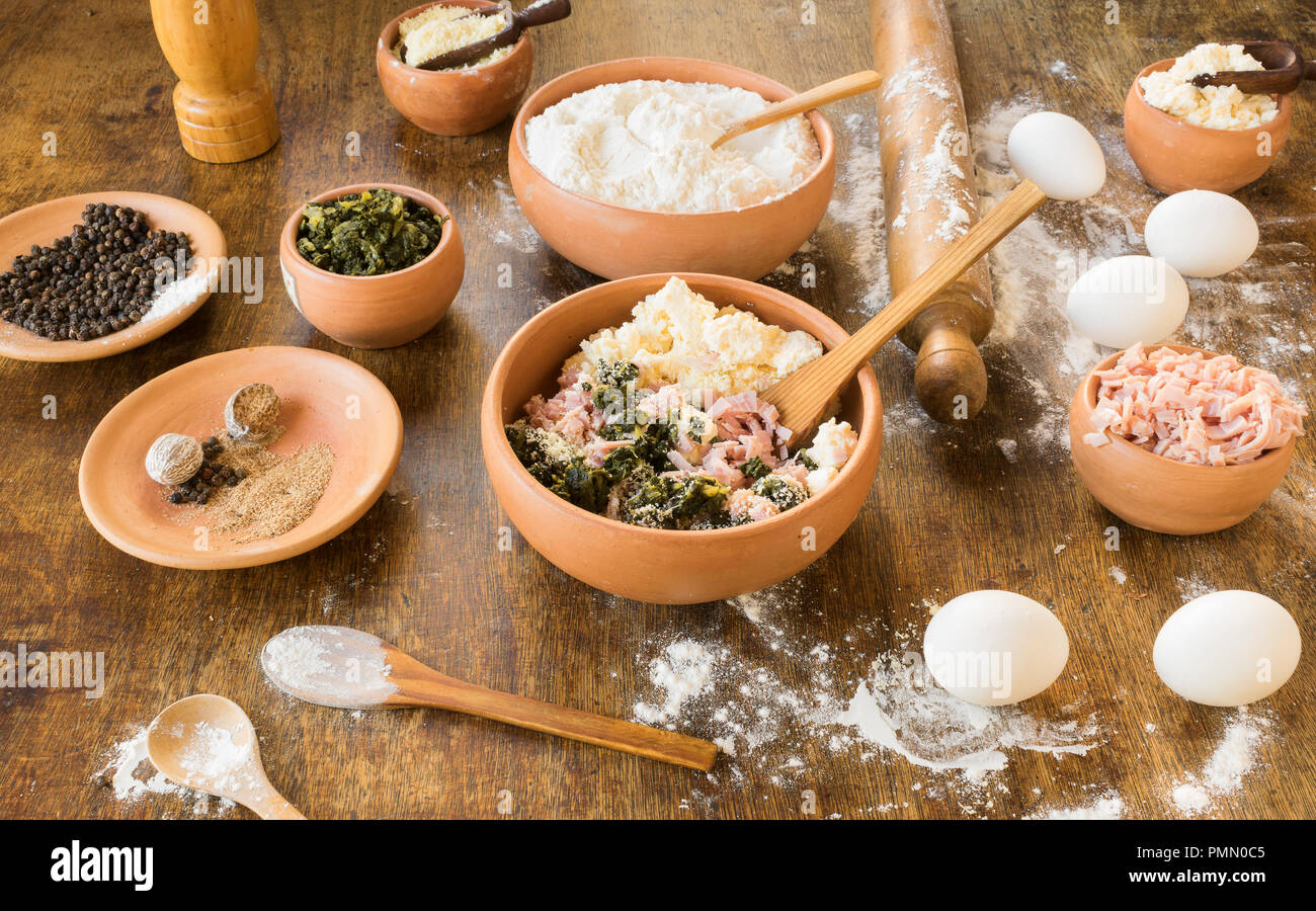 Des ingrédients pour préparer des pâtes farcies comme les ravioli ou tortellini : blettes, jambon, fromage, la ricotta, la farine, les œufs, la muscade et le poivre avec la cuisine rustique Banque D'Images
