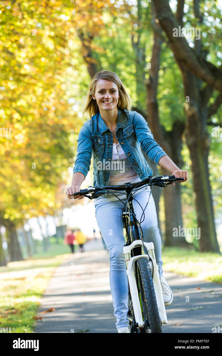 Jeune femme faire du vélo dans le parc de l'automne. Tout en appréciant à vélo dans la nature au cours de journée d'automne. Banque D'Images