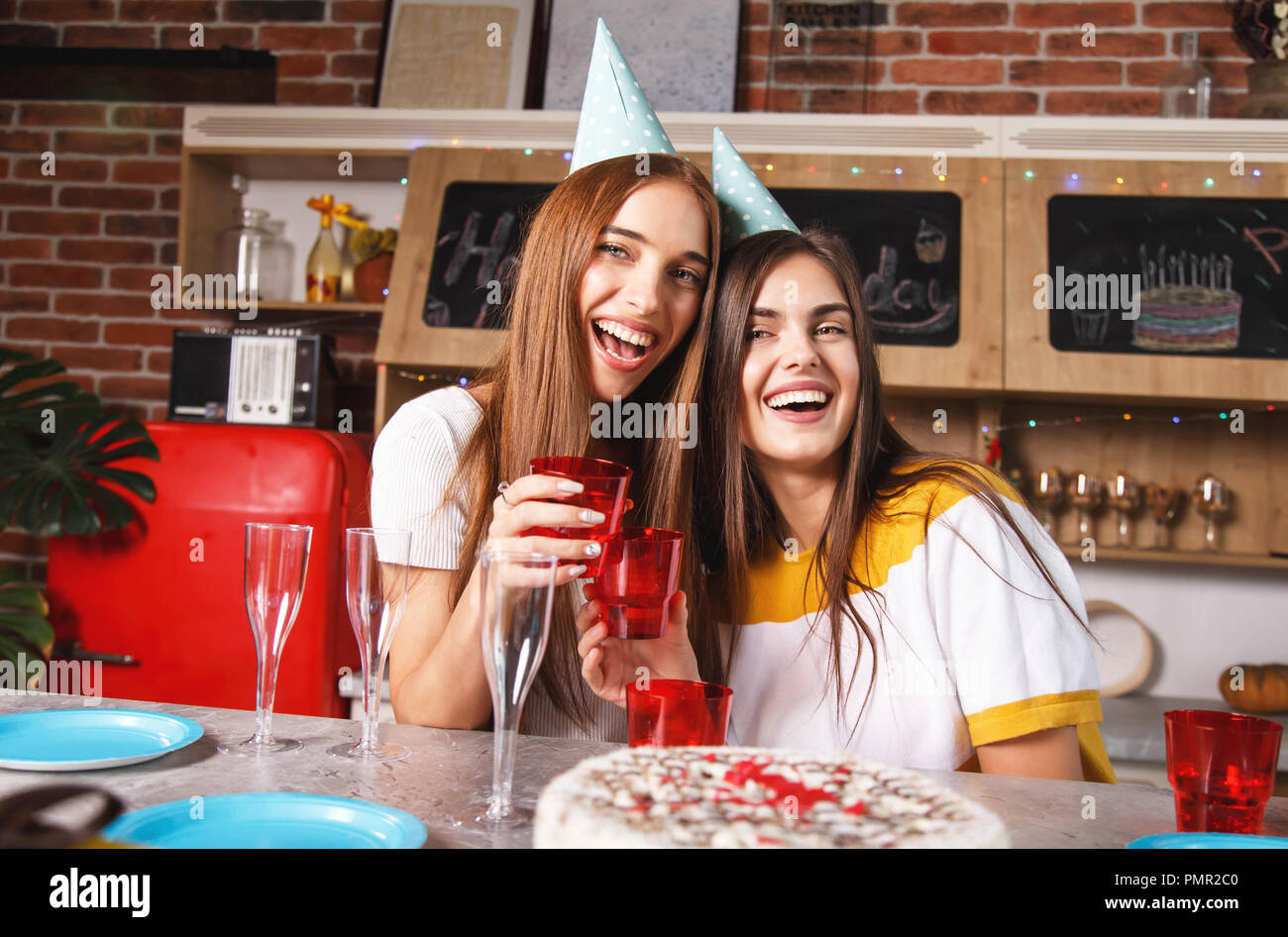 Brunette copines dans les chapeaux de fête holding drinks et celebrating birthday Banque D'Images
