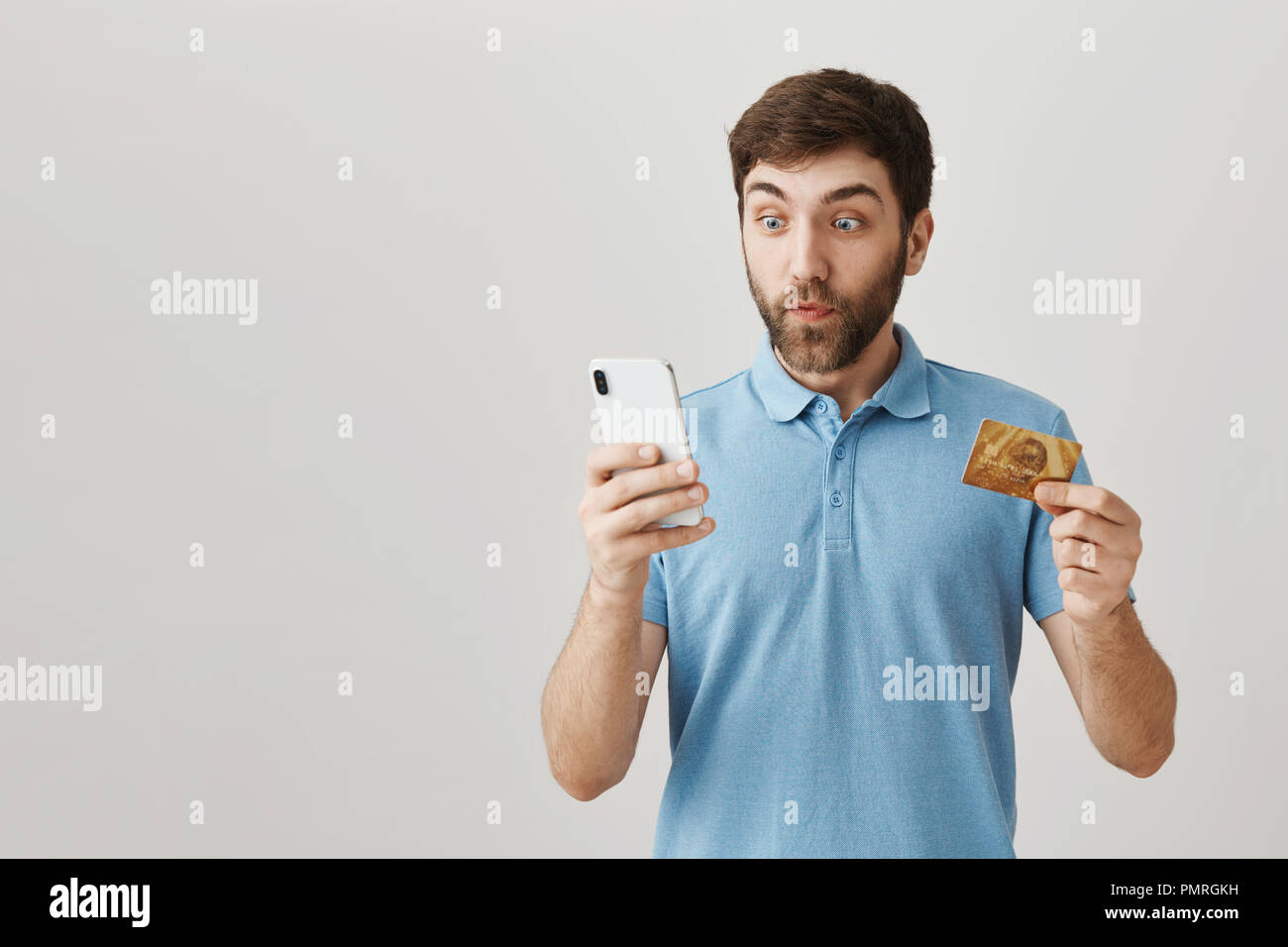 Qu'est-ce que cette carte de crédit peut faire. Studio shot of excité et choqué employé, montrant la carte de crédit à huis clos tout en maintenant l'écran du smartphone et à la recherche sur l'expression impressionnée avec Banque D'Images