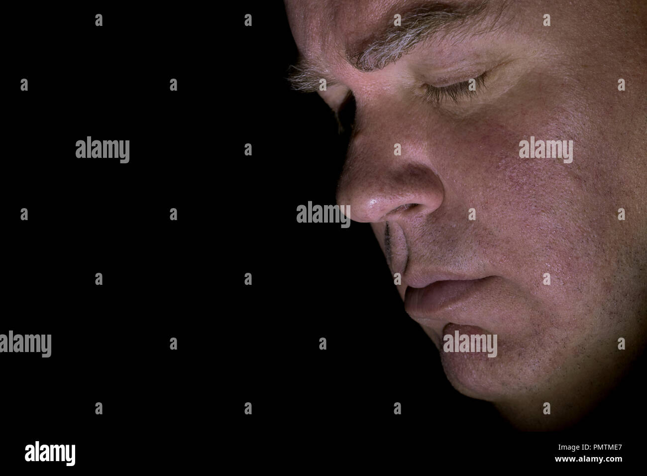 Image Gros plan de parution du modèle de race blanche d'âge moyen visage de l'homme avec les yeux fermés, à la triste et solennel, vue latérale avec un fond noir. Banque D'Images