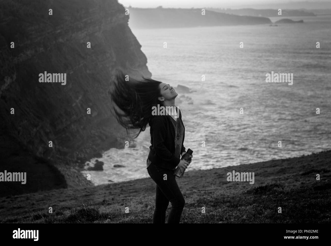 Jeune femme se balançant et soufflé les cheveux longs par le vent dans une falaise lors d'une randonnée dans la nature au coucher du soleil Banque D'Images