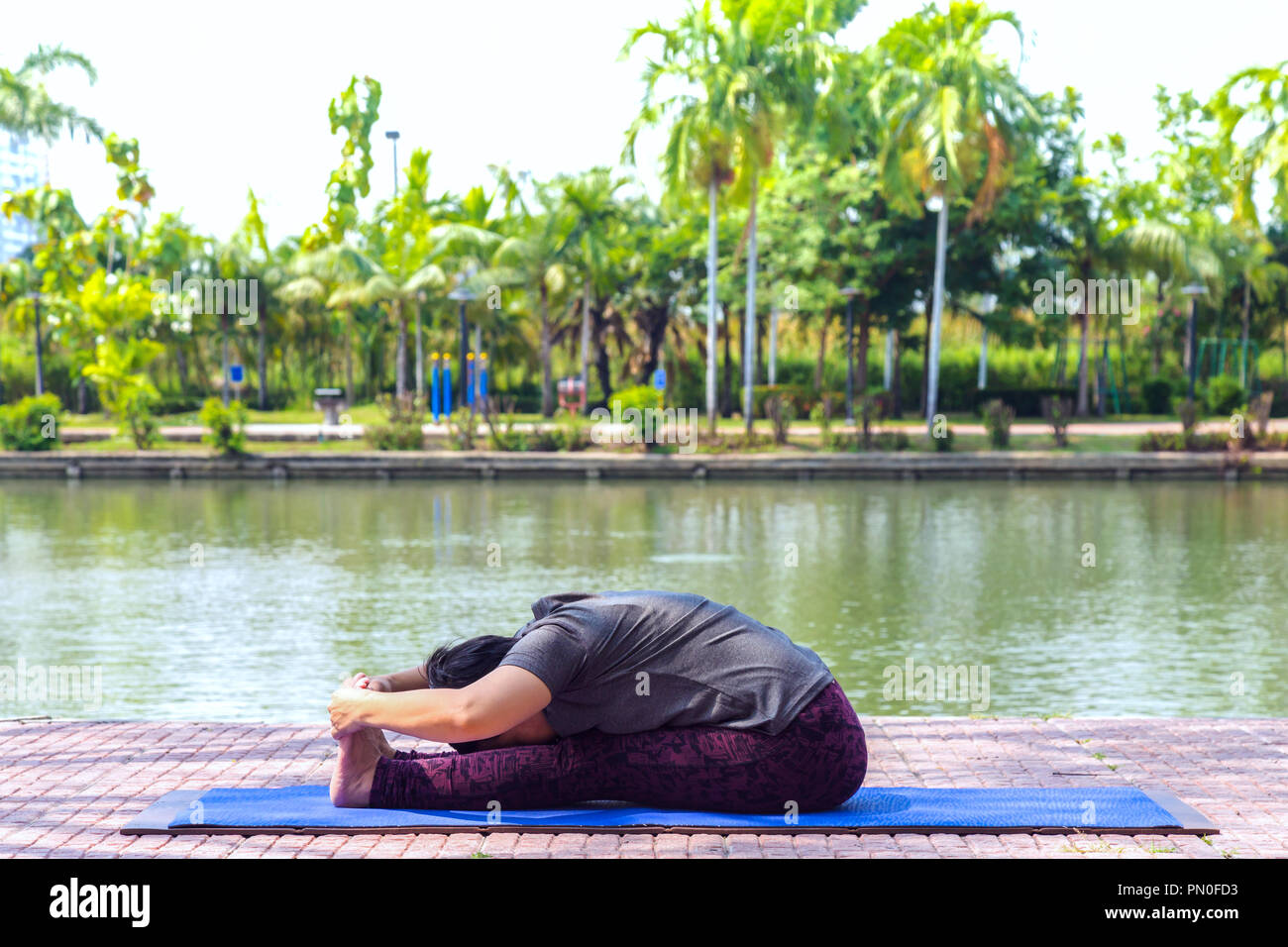 D'âge moyen en bonne santé asian woman sitting in assis vers l'exercice ou paschimottanasana yoga pose au parc de la ville à le matin. en bonne santé et lifest Banque D'Images